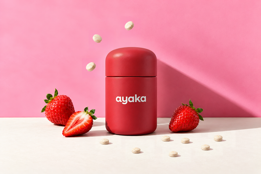 The red Ayaka jar, strawberries and chewable tablets against a pink wall.